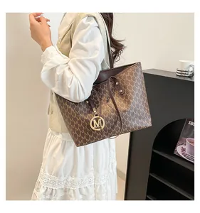 Detail of coffee brown tote bag with repeating M pattern and gold metal charm