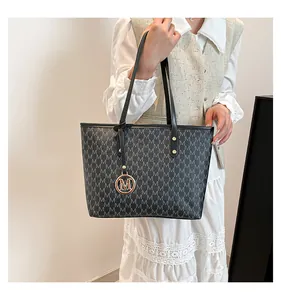Detail of grey monogram tote bag with gold M pendant and premium leather texture