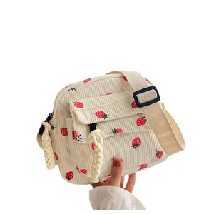 Cream corduroy crossbody bag with strawberry print and decorative woven pendant