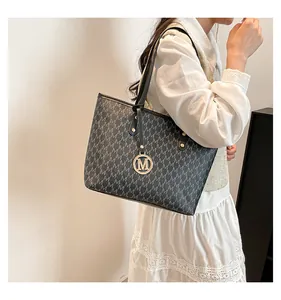 Detail showing dark grey tote bag with monogram print and golden metal M pendant