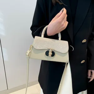 Elegant cream shoulder bag with rhinestone flap and gold T-clasp held by a model