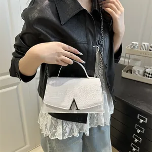 White crocodile-embossed handbag with silver V-logo and metal chain strap held by model