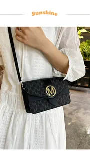 Detail shot of a black crossbody bag with M-pattern and gold logo on white dress