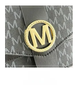Close-up of golden circular M-logo and printed leather texture on black crossbody bag