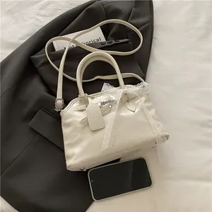Détail d'un sac à main beige avec nœud en dentelle et pieds de protection en argent