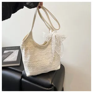 Detail einer cremefarbenen Spitzen-Schultertasche mit dekorativer Schleife und Webmuster