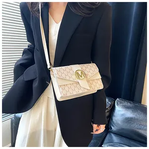 Close-up of a beige crossbody square bag with 'M' monogram pattern and gold buckle