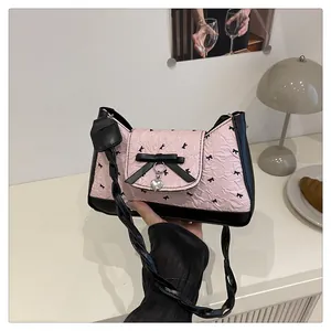 Détail du sac sous le bras plissé rose avec nœud noir, breloque cœur et anse tressée