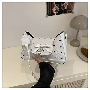 Détail du sac baguette blanc avec motifs de nœuds et pendentif coeur en argent