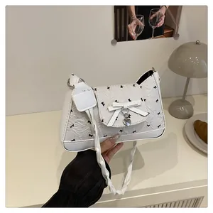 Détail du sac à bandoulière plissé crème avec petits nœuds noirs et pendentif cœur