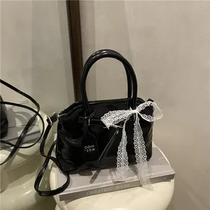 Détail du sac en cuir verni noir brillant avec nœud en dentelle blanche et étiquette