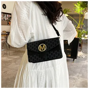 Detail of black flap shoulder bag with M pattern and golden metal buckle on model