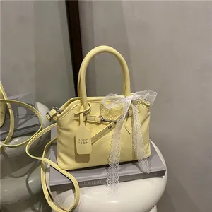 Détail du sac à bandoulière jaune pâle avec nœud en dentelle blanche et étiquette de marque