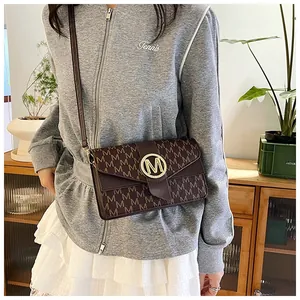 Detail shot of a brown crossbody bag with M-pattern print and a large golden metal buckle