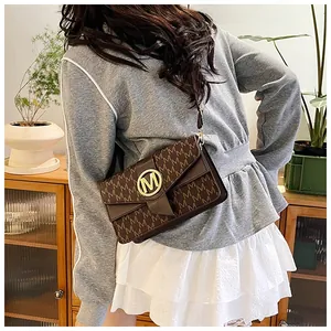Detail shot of brown monogram crossbody bag with gold M buckle worn by a model