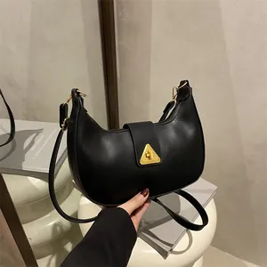Minimalist black crescent shoulder bag with gold triangle clasp on a modern pedestal
