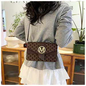 Detail of a brown monogram crossbody bag with gold M-buckle on a stylish outfit