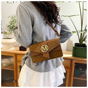 Brown vintage messenger bag with M monogram pattern and gold metal clasp worn by a model