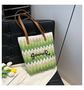 Dettaglio della borsa tote intrecciata con motivi a onde verdi e manici in pelle su divano