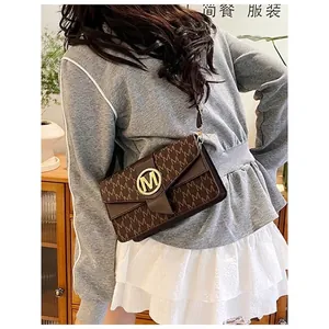 Brown monogram crossbody bag with gold M buckle worn by a model in casual style