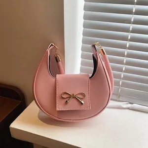Sac hobo rose pastel à texture Saffiano avec un nœud doré sur un rebord de fenêtre blanc