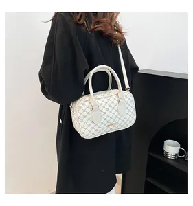 Détail du sac Boston avec motif de chaîne et bandoulière réglable sur un sac crème