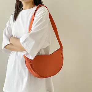 Detail of burnt orange nylon crescent crossbody bag worn by model over white t-shirt
