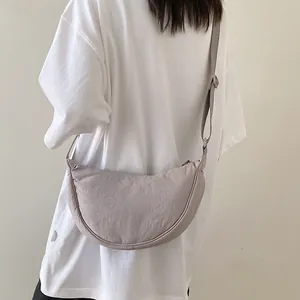 Detail of a beige nylon dumpling crossbody bag worn on shoulder with adjustable strap