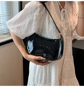 Borsa a spalla in vernice nera lucida indossata da modella con abito bianco