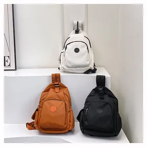 Drei Nylon-Umhängetaschen in Creme, Orange und Schwarz auf einer weißen Treppe