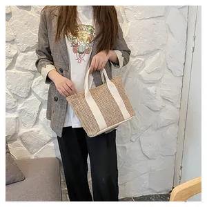 Detail of woven straw tote bag with beige striped handles for summer vacation beach look