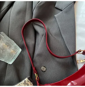 Detail of burgundy patent leather shoulder bag with glossy texture and gold hardware