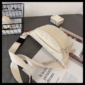 Macro detail of cream corduroy chest bag featuring textured fabric and knotted zipper pull