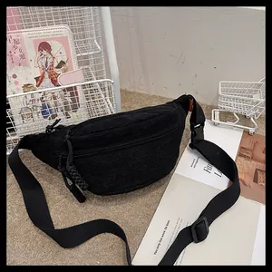 Close-up of black corduroy belt bag with woven rope zipper pulls on a cozy rug