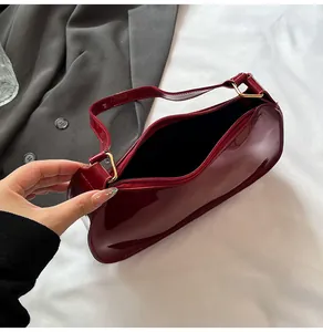 Detail of burgundy glossy faux leather underarm bag with zipper closure on grey fabric