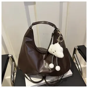 Detail view of deep brown faux leather tote bag with a cute plush cloud charm and strap
