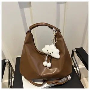 Detail of brown matte leather hobo bag with cloud charm on a minimalist leather chair