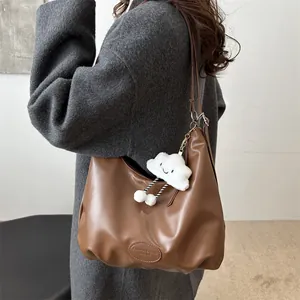Brown leather tote bag with cloud charm accessory worn by model over a grey coat