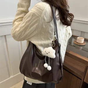 Large dark brown leather tote bag with cloud plush charm shown from a side-rear angle