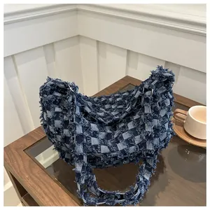 Gros plan du sac bandoulière en denim à damier avec texture effilochée sur table