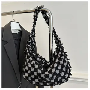 Détail du sac hobo en denim à damier noir et blanc avec bords effilochés sur un cintre