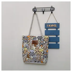 Detail of canvas tote bag with colorful cat prints and braided rope handle on a hook