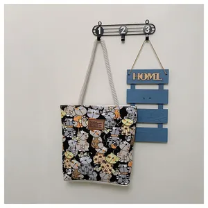 Detail of cartoon cat canvas tote bag featuring cotton rope handles and leather logo patch
