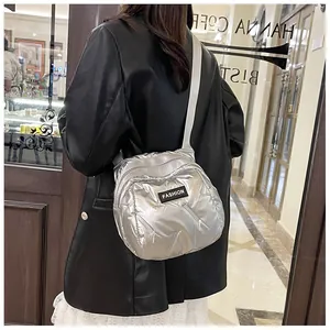 Detail of silver metallic quilted puffer crossbody bag with fashion label and wide strap