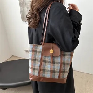 Stylish plaid tote bag with brown leather trim and golden N buckle worn over the shoulder
