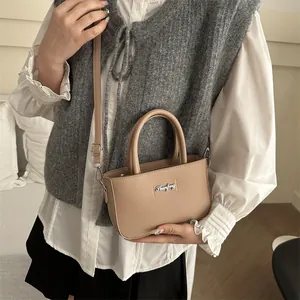 Minimalist light brown crossbody bag with silver hardware held by model in casual outfit