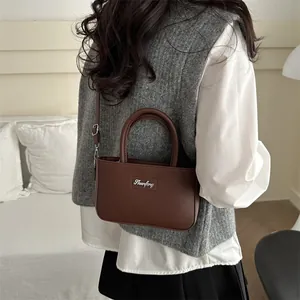 Minimalist dark brown crossbody bag with silver logo and top handle in a cozy indoor setting
