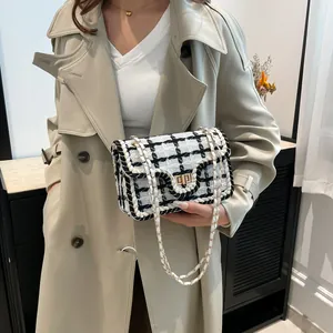 Elegante zwart-witte tweed schoudertas met gouden ketting gedragen door een model