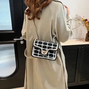 Klassieke zwart-witte geruite tweed crossbodytas met gouden ketting op beige jas