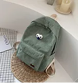 Detailed view of green corduroy backpack with cute cartoon eyes on woven straw mat